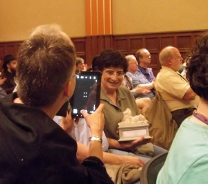 Susan Palwick uses her iPad to take a photo of Lisa Goldstein with her Mythopoeic Fantasy Award lion statuette, at the Mythcon 43 post-banquet award presentations. (Photo by Lynn Maudlin)